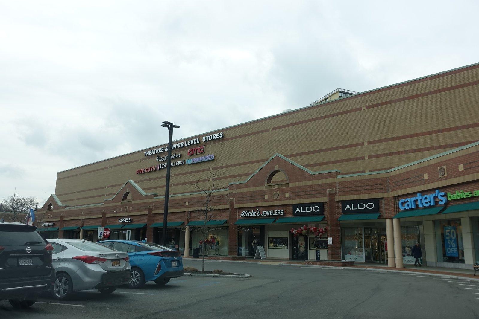 Bay Terrace shopping center’s brick shopfronts below the cinema building and AMC sign, February 2022.