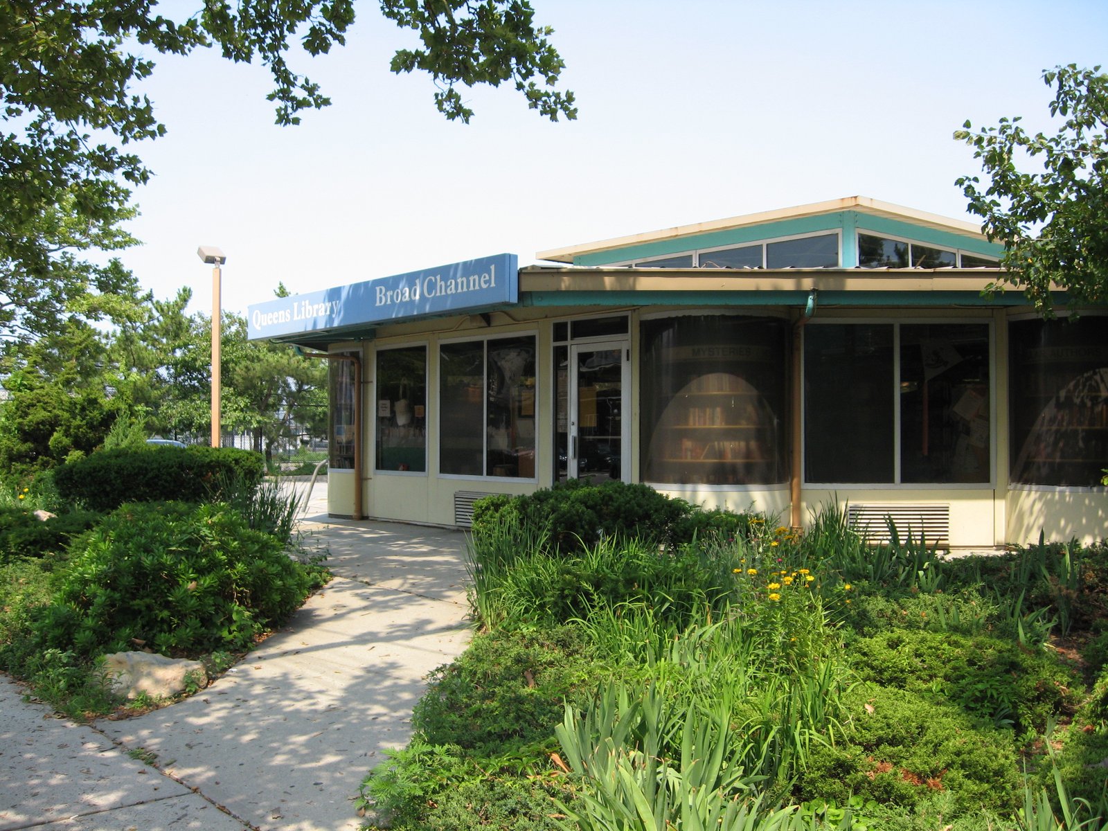 The low Broad Channel Library building with its turquoise sign, glass entrance and planted path.