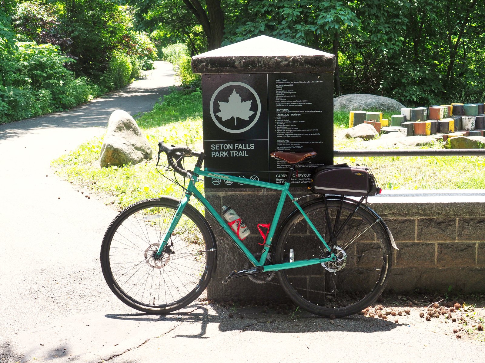 Seton Falls Park Trail entrance sign beside a wooded path, with a bicycle in front.