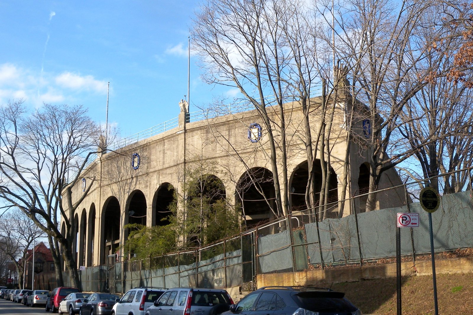 The arched concrete exterior of Forest Hills Stadium with blue crest medallions and flagpoles.
