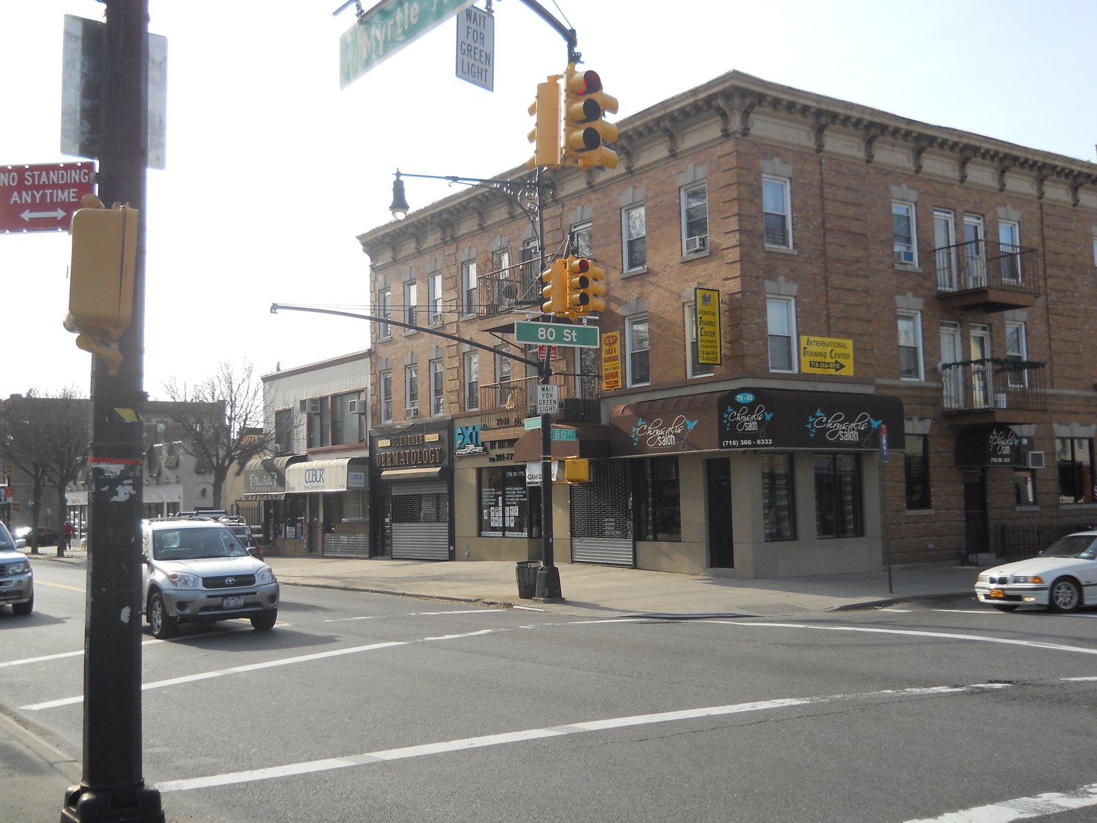 Myrtle Avenue and 80th Street in Glendale, with a brick corner building, storefronts and traffic lights.