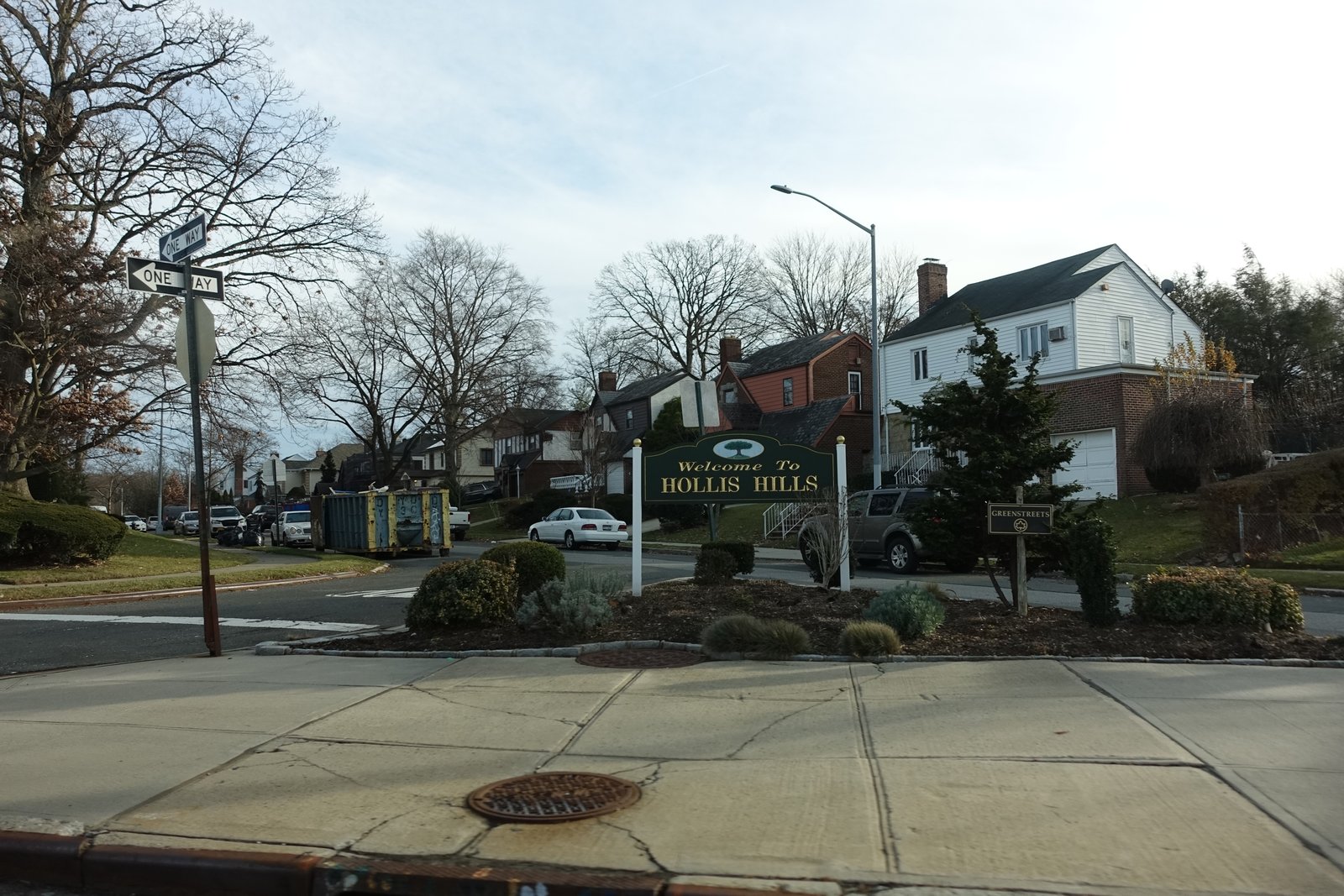 Hollis Hills welcome sign in a planted triangle with detached houses behind, December 2021.