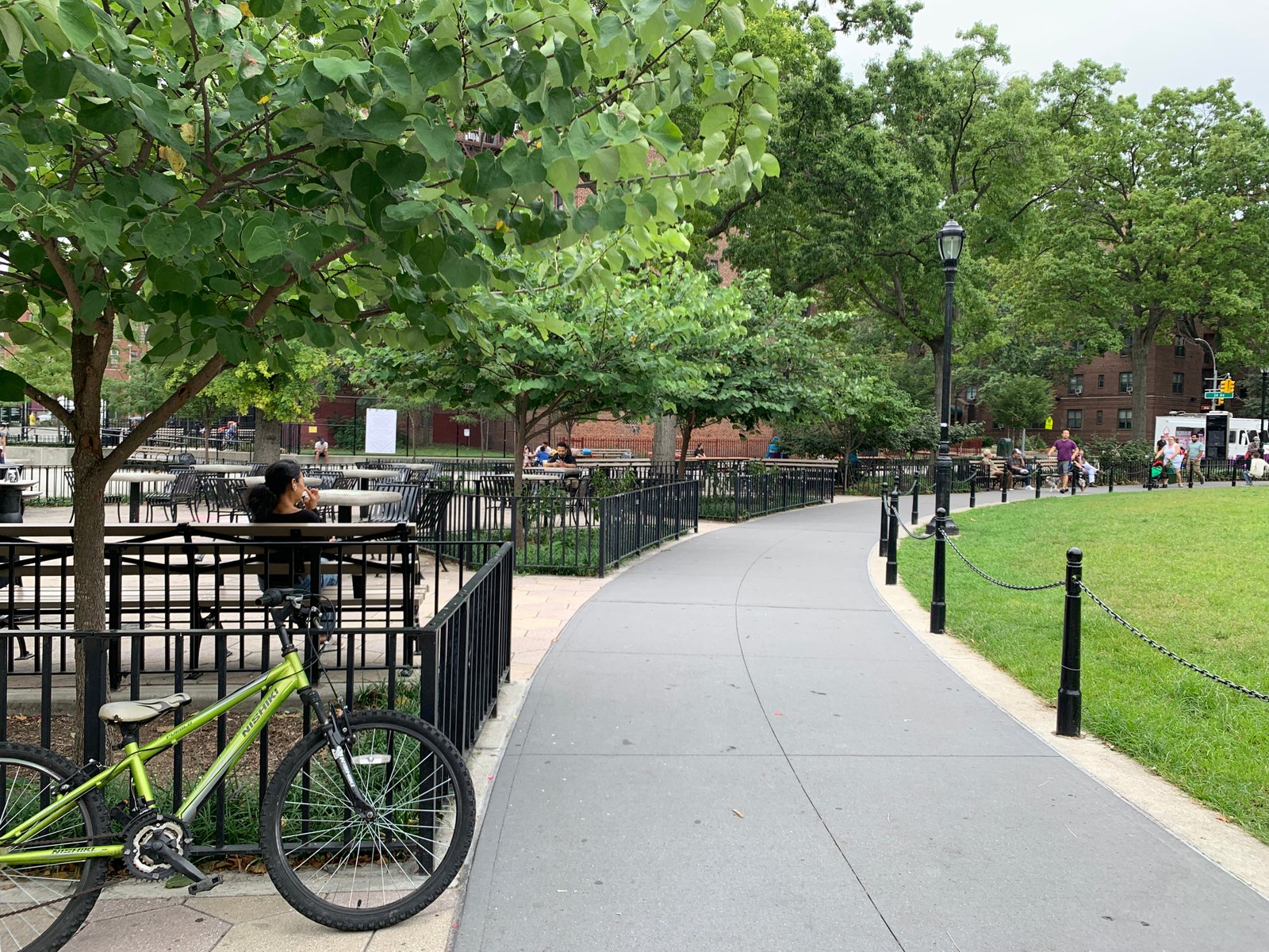 A curved path beside the lawn at Travers Park, with benches, trees and visitors.