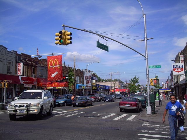 Historical commercial street scene at Liberty Avenue and Lefferts Boulevard, with both street signs visible.