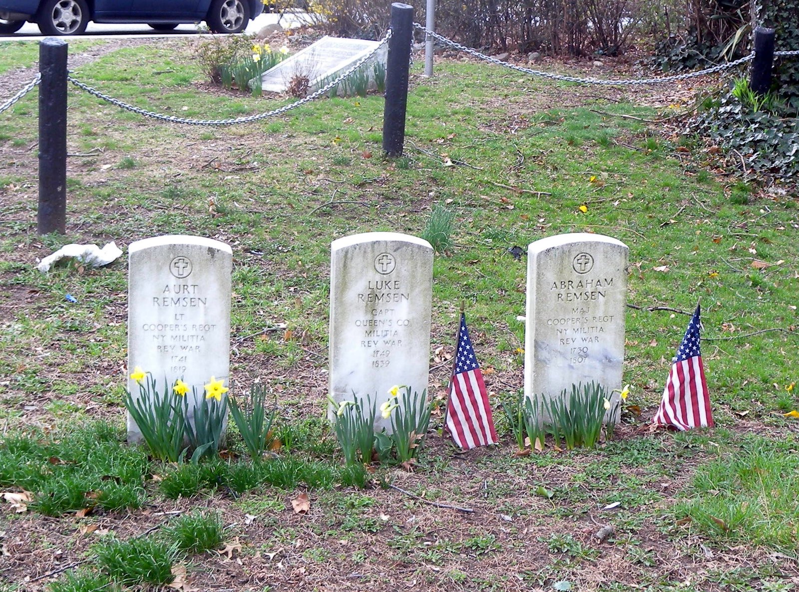 Three pale Remsen family commemorative grave markers with small flags and daffodils, March 2010.