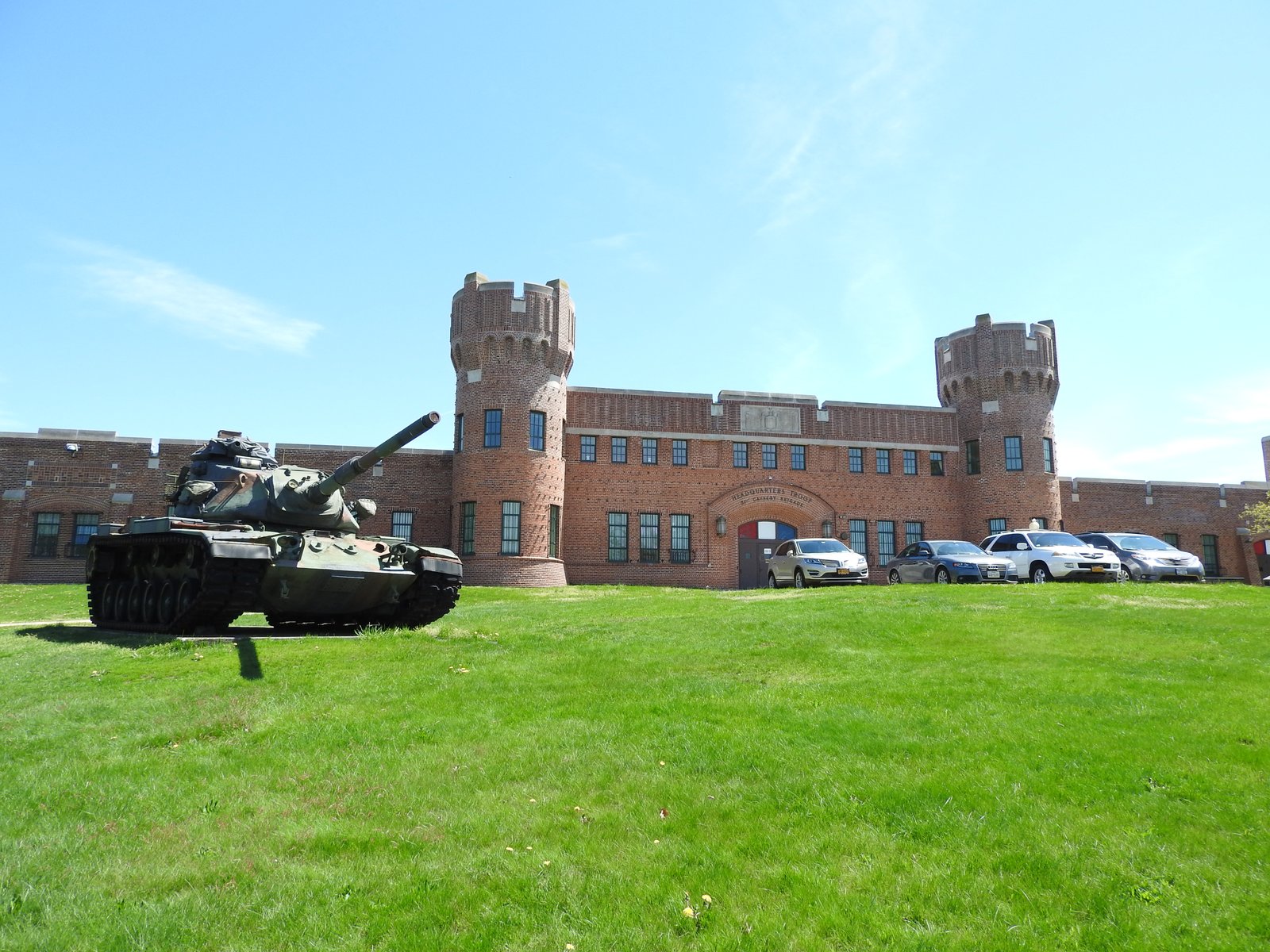 Brick armory at 321 Manor Road in 2017, with round towers, crenellated parapets and a tank on the lawn.