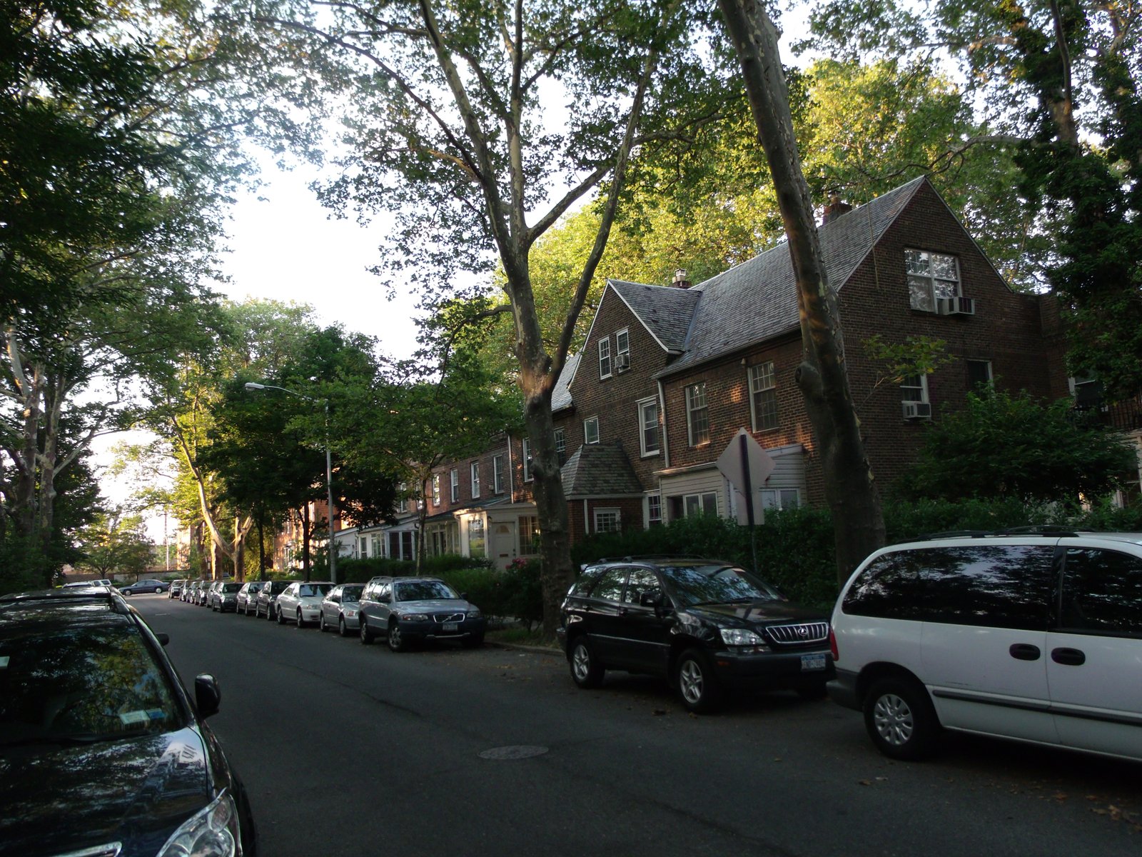 Brick Sunnyside Gardens row houses with pitched roofs along a tree-lined street.
