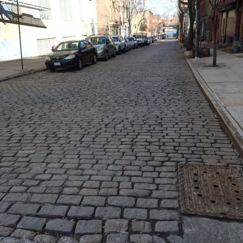 A cobbled street runs between brick buildings and parked cars in Vinegar Hill.