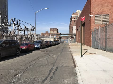 Electrical equipment lines Hudson Avenue opposite brick industrial buildings.