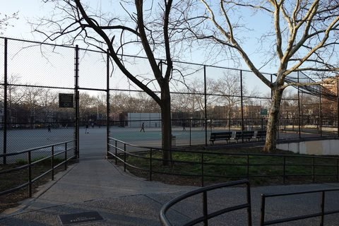 A path leads past trees and fencing to the courts at Greenwood Playground.