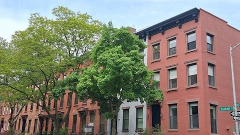 Brick row houses and trees at a Carroll Gardens street corner.