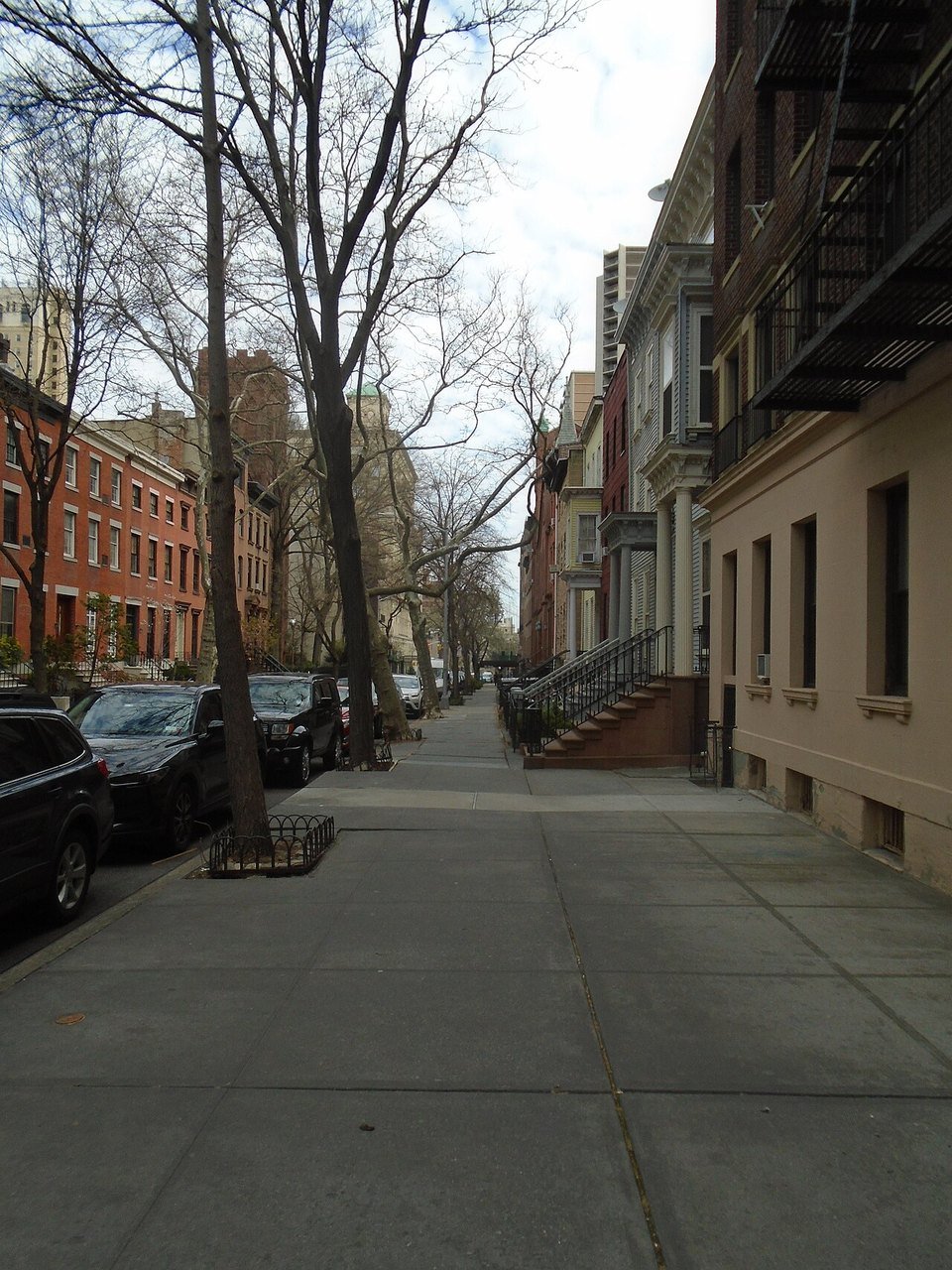 A Cobble Hill sidewalk beside row houses, parked cars and leafless trees.