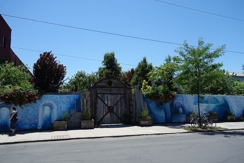 A painted wall and a closed gate outside the Pioneer Works garden, with trees behind them in 2018.