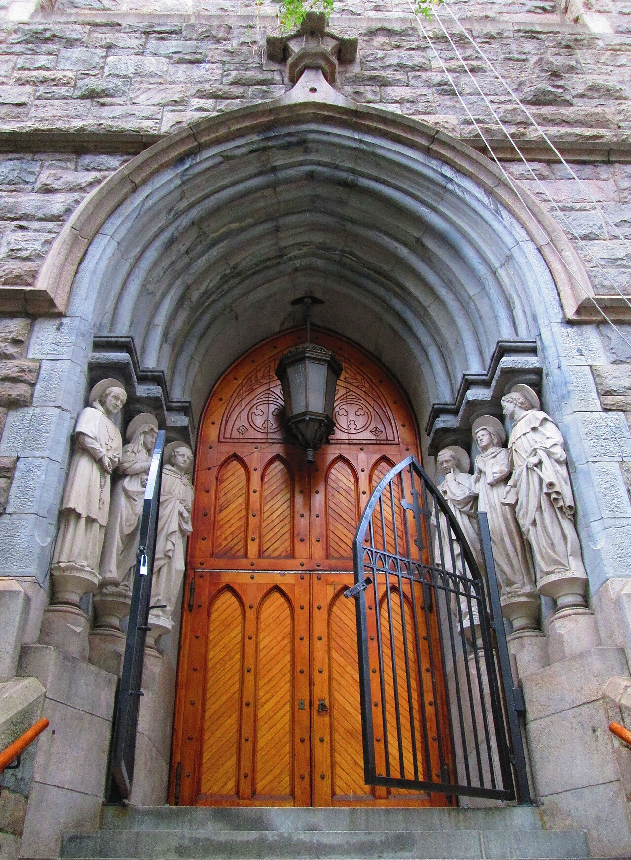 North entrance detail of St. Paul the Apostle, with its stone arch, carved saints and wooden doors in 2014