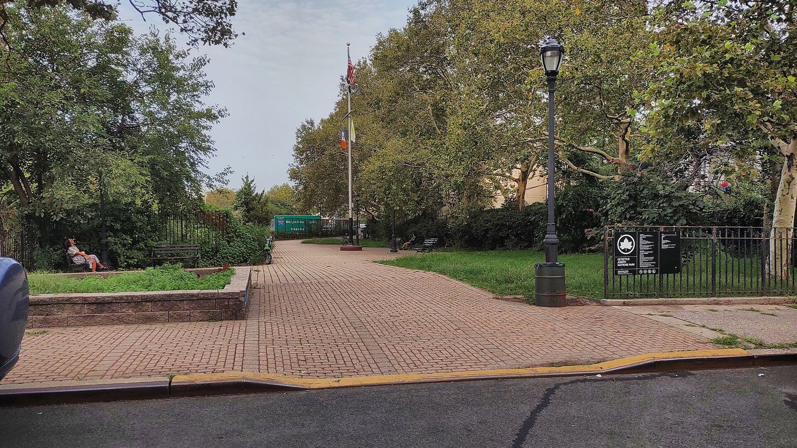 A paved path leads into a small park with trees and benches.